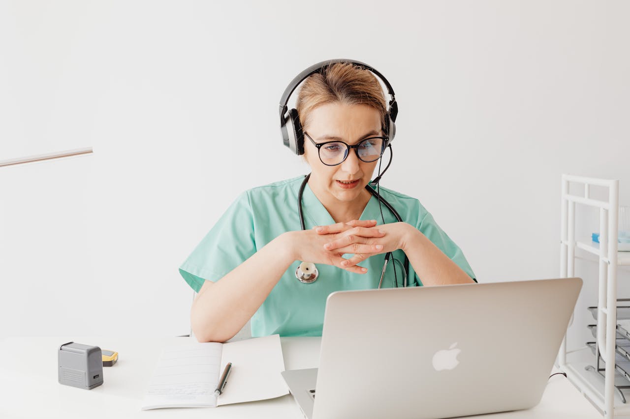 about-bg Doctor in scrubs having an online video call from her office, wearing headphones.