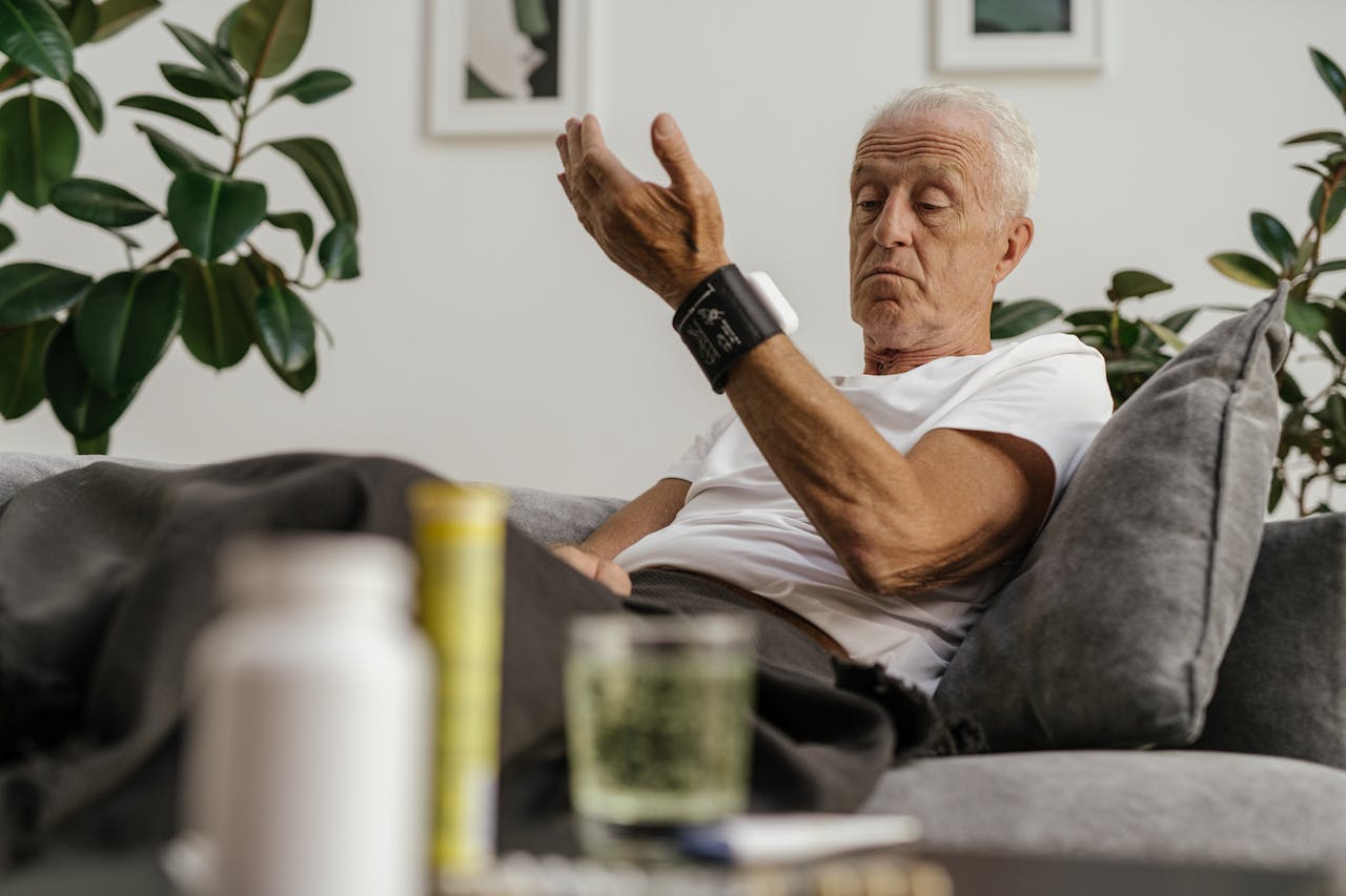 services-06 Elderly man checks his blood pressure using a wrist monitor in a comfortable living room setting.
